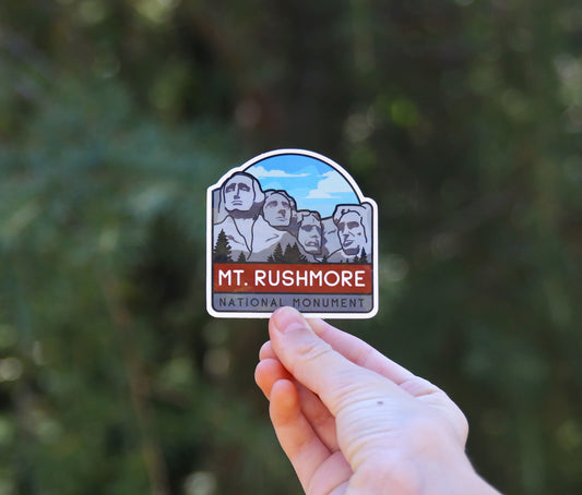 Held a little further back, the Mt. Rushmore National Monument sticker shows four carved faces and blue sky.