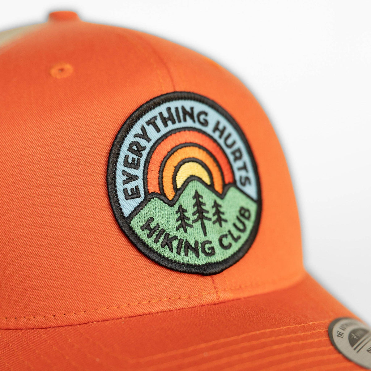 Sunrise arcs in orange and yellow on the patch stitched to the orange Hiking Club trucker hat crown.