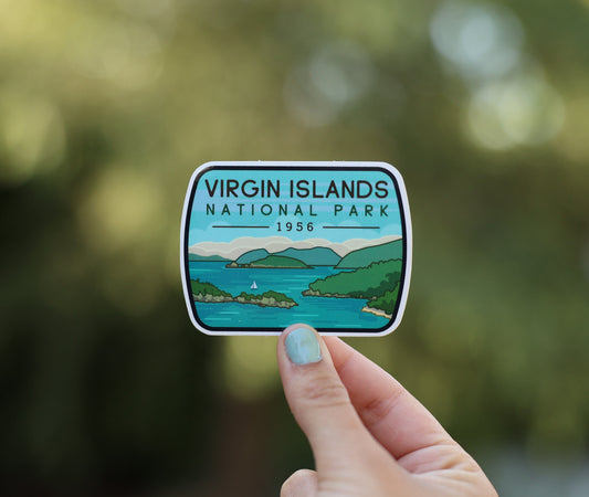 Held farther back, the Virgin Islands National Park sticker shows its sailboat and turquoise bay in soft daylight.
