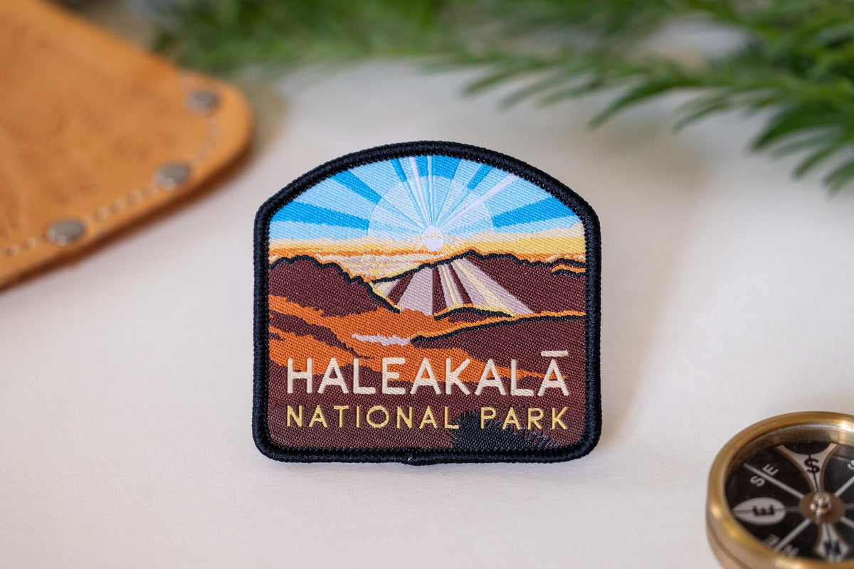 Beside a leather sheath and brass compass, the Haleakala National Park patch shows its sunrise crater stitching.