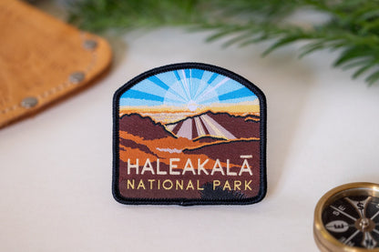 Beside a leather sheath and brass compass, the Haleakala National Park patch shows its sunrise crater stitching.
