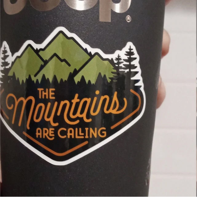 Close on a black Jeep tumbler, The Mountains Are Calling sticker wraps slightly with the curve.