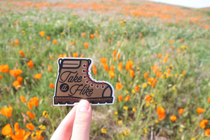 Held closer to the camera, the Take a Hike sticker stands crisp against a poppy covered hillside.