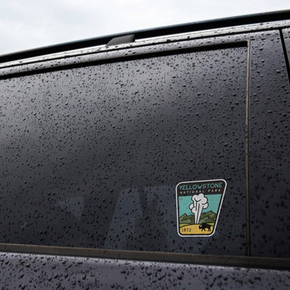 Rain beads across a black car window where the Yellowstone National Park sticker is applied near the frame.