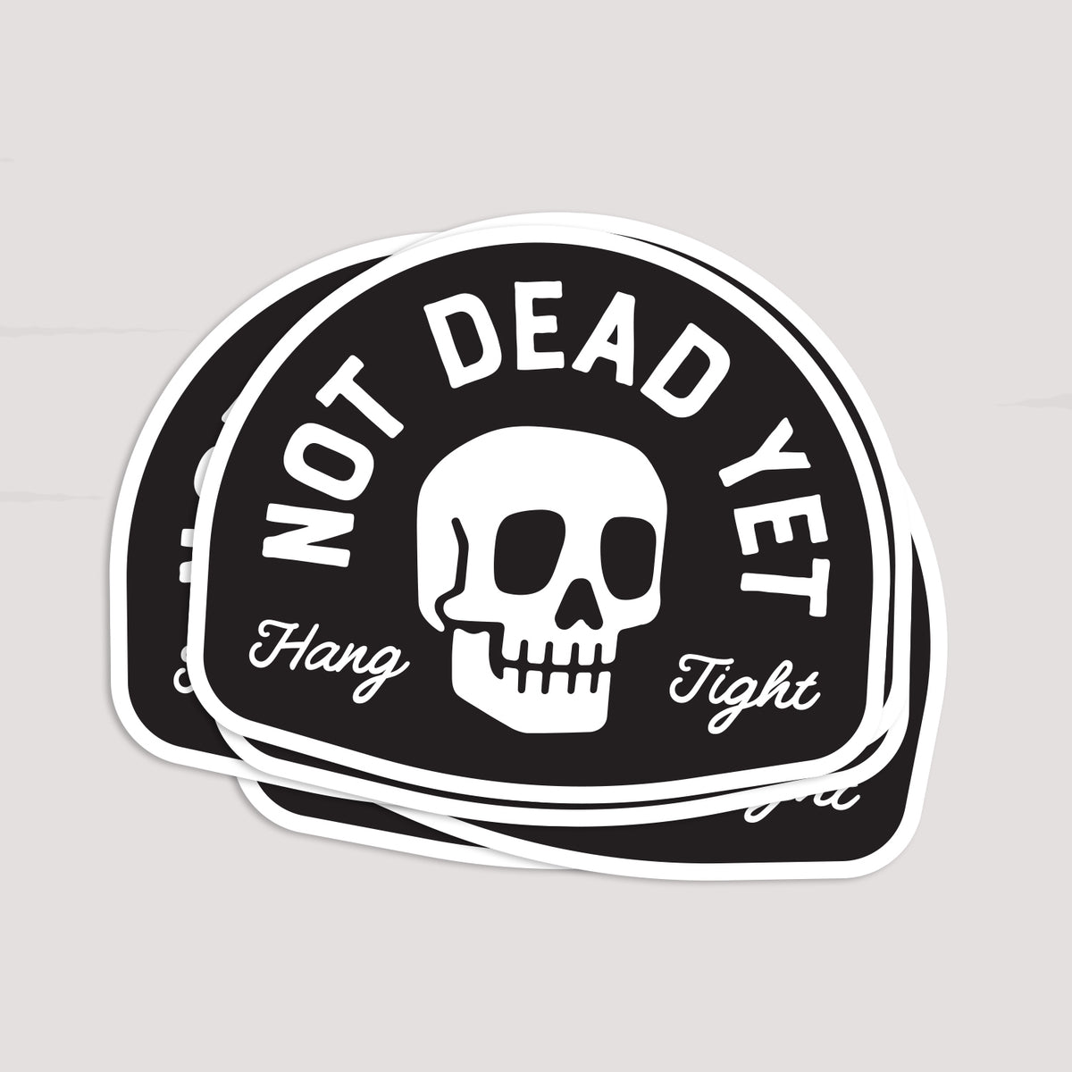 Several Not Dead Yet stickers lie stacked together, their white borders overlapping in a loose fan.