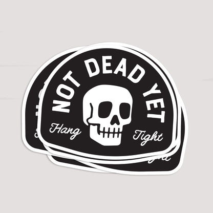 Several Not Dead Yet stickers lie stacked together, their white borders overlapping in a loose fan.