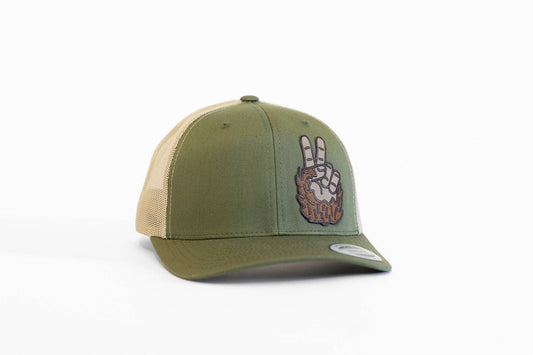 Angled on a white backdrop, the olive Bigfoot Peace Left Side Trucker Hat shows its furry hand patch and tan mesh.