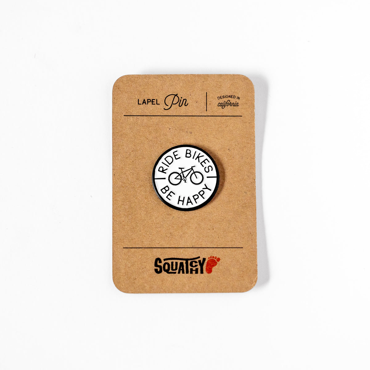 Displayed on its kraft paper card, the Ride Bikes Be Happy lapel pin sits above the Squatchy logo stamp.