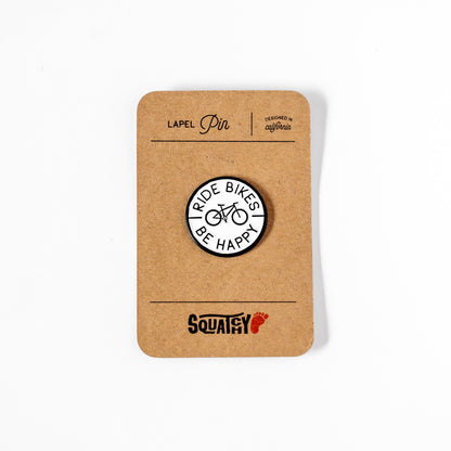 Displayed on its kraft paper card, the Ride Bikes Be Happy lapel pin sits above the Squatchy logo stamp.