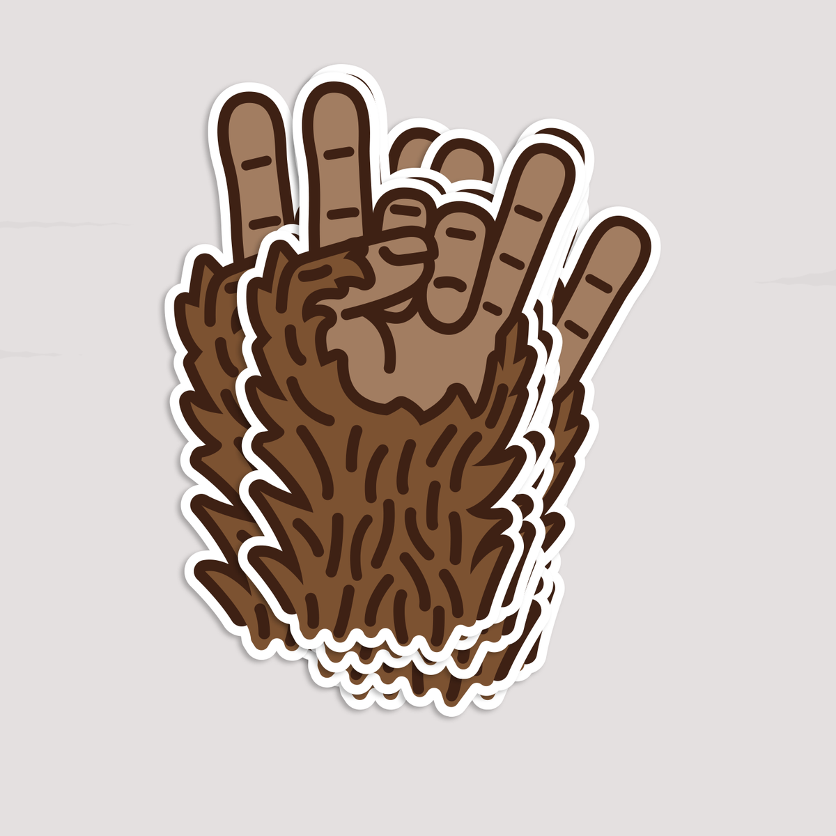 Two Bigfoot Rocks stickers overlap on a grey backdrop, showing the hairy hand and raised fingers.