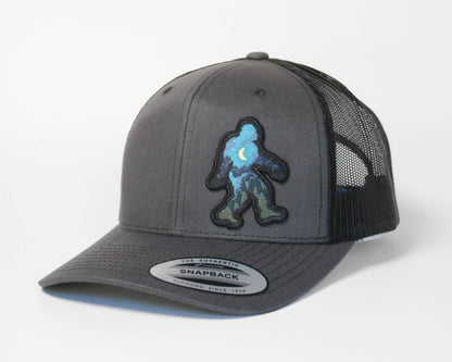 Charcoal grey Bigfoot Night Sky trucker hat with black mesh, the moon and pine patch straight on at the front.