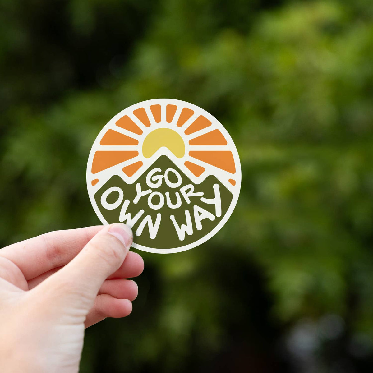 Held low in the frame, the Go Your Own Way sticker shows its mountain and sunburst against leafy green.
