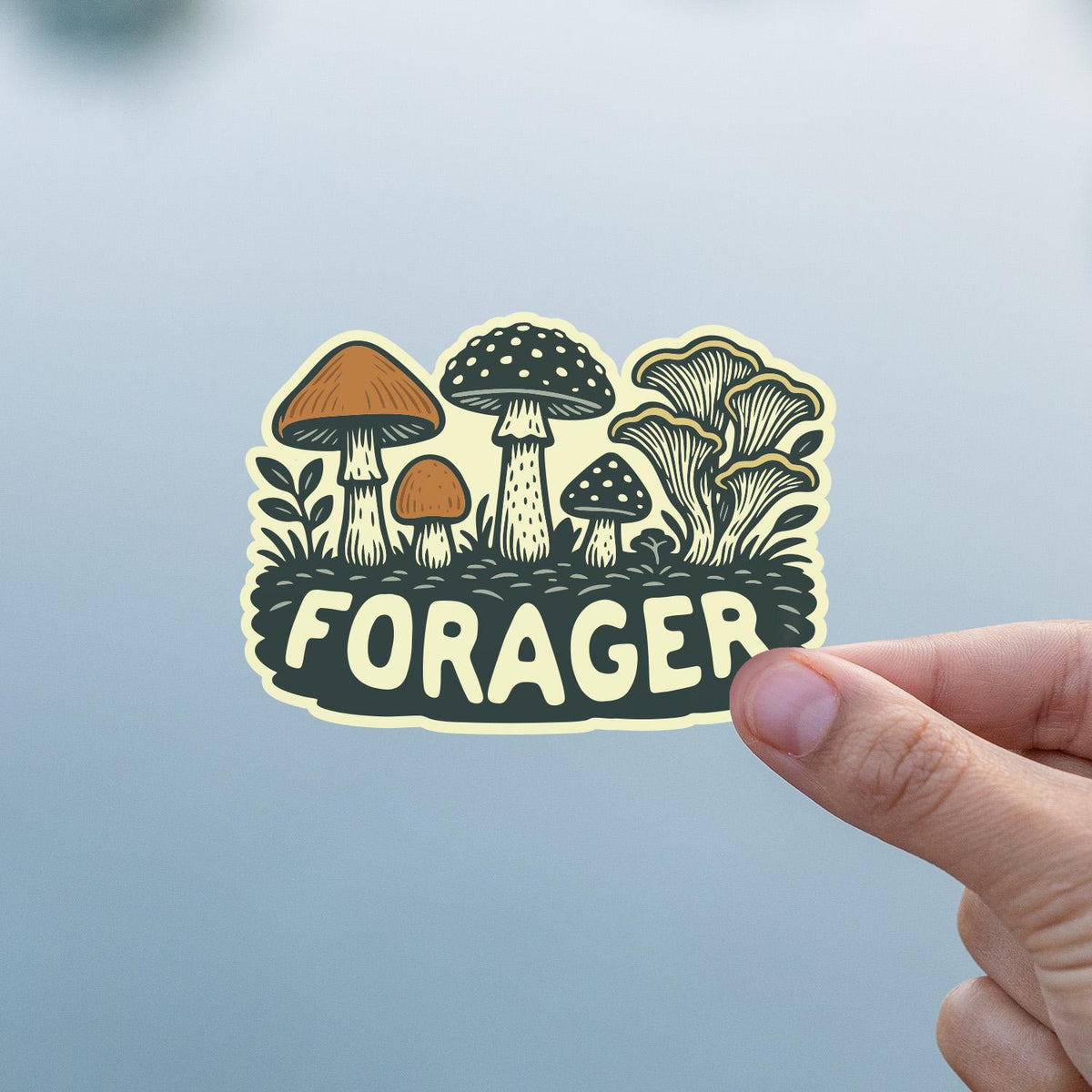 Close and cropped, a thumb steadies the Forager Mushrooms sticker against a pale blue grey blur.