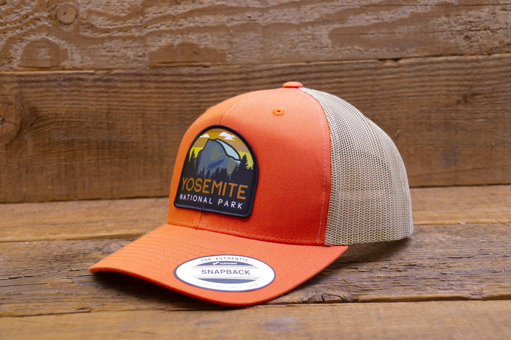 Against grey barn boards, the orange Yosemite National Park trucker hat shows off its khaki mesh back.