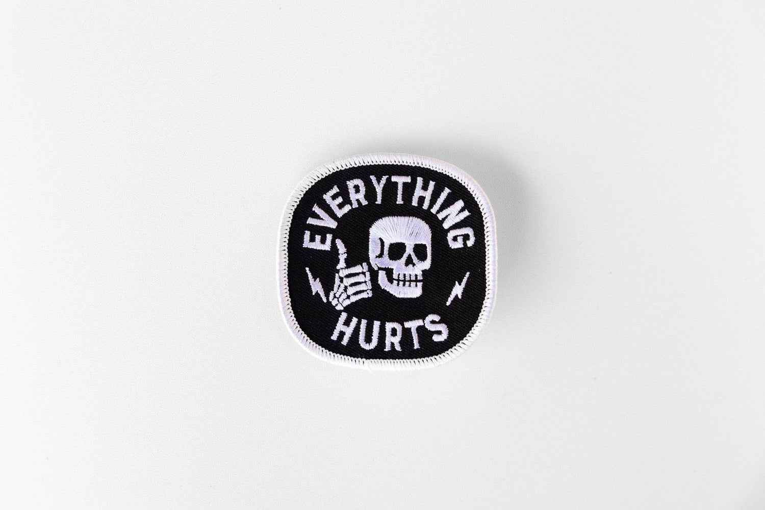 Centered on a plain white surface, the Everything Hurts patch shows a skull and thumbs up in white stitching.