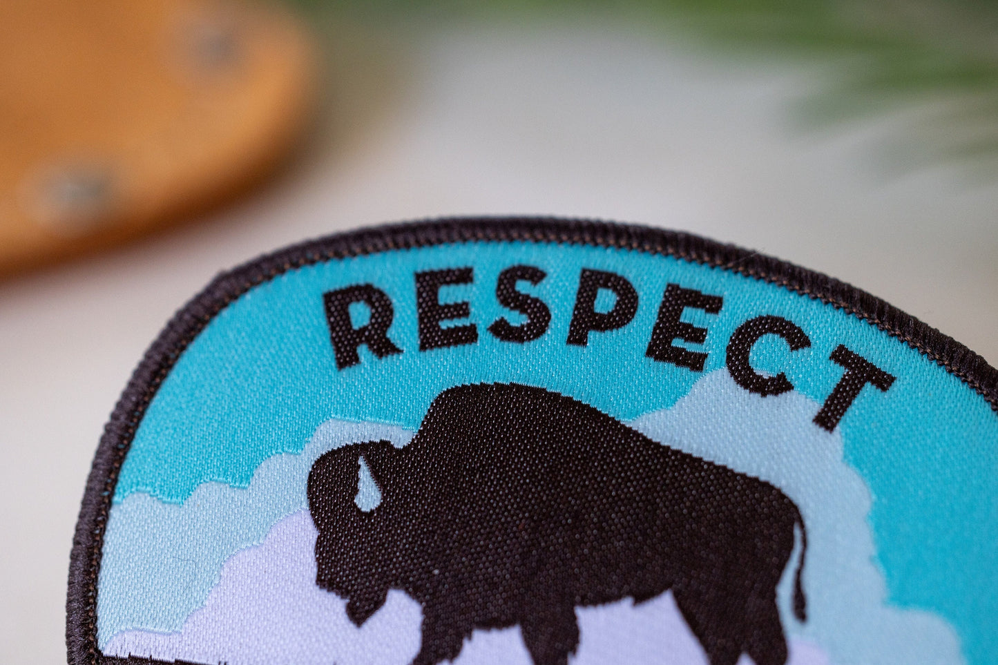 Cropped tight on the stitching, the bison and the word RESPECT fill the patch beside a blurred wood coaster.
