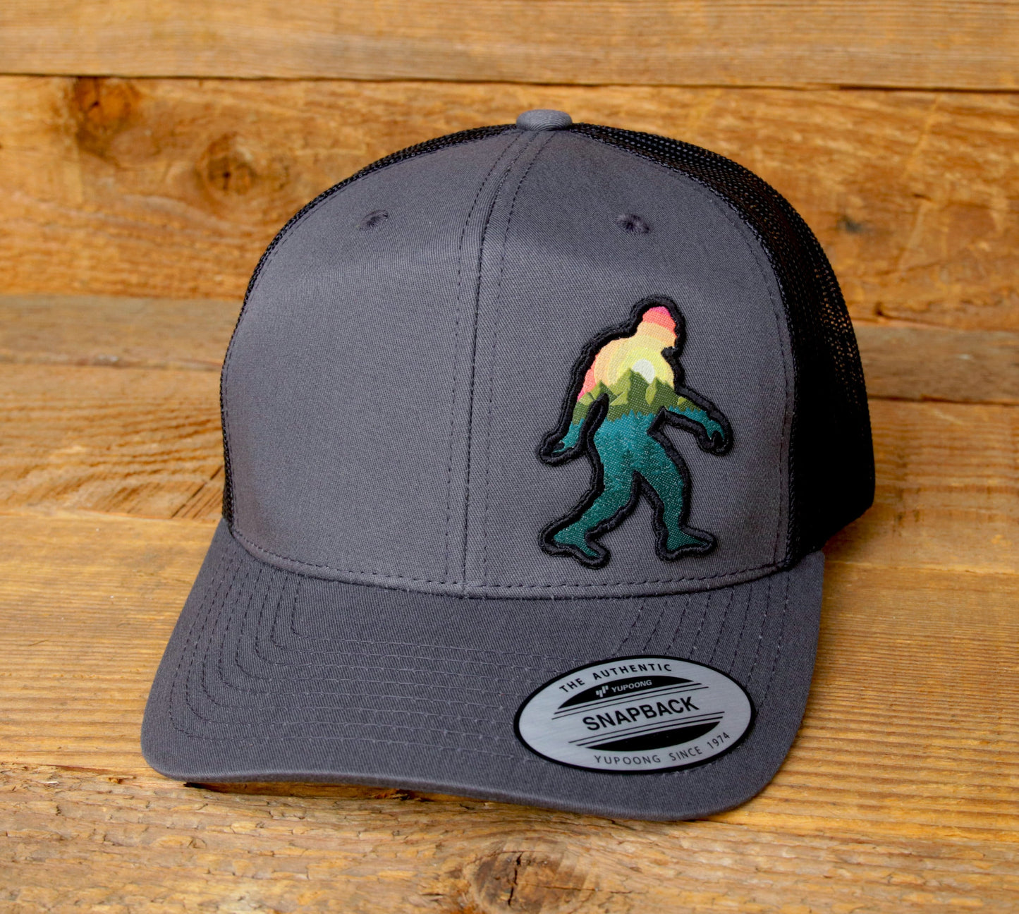 Resting on weathered wood planks, the grey Bigfoot Adventure trucker hat faces forward with patch centered.