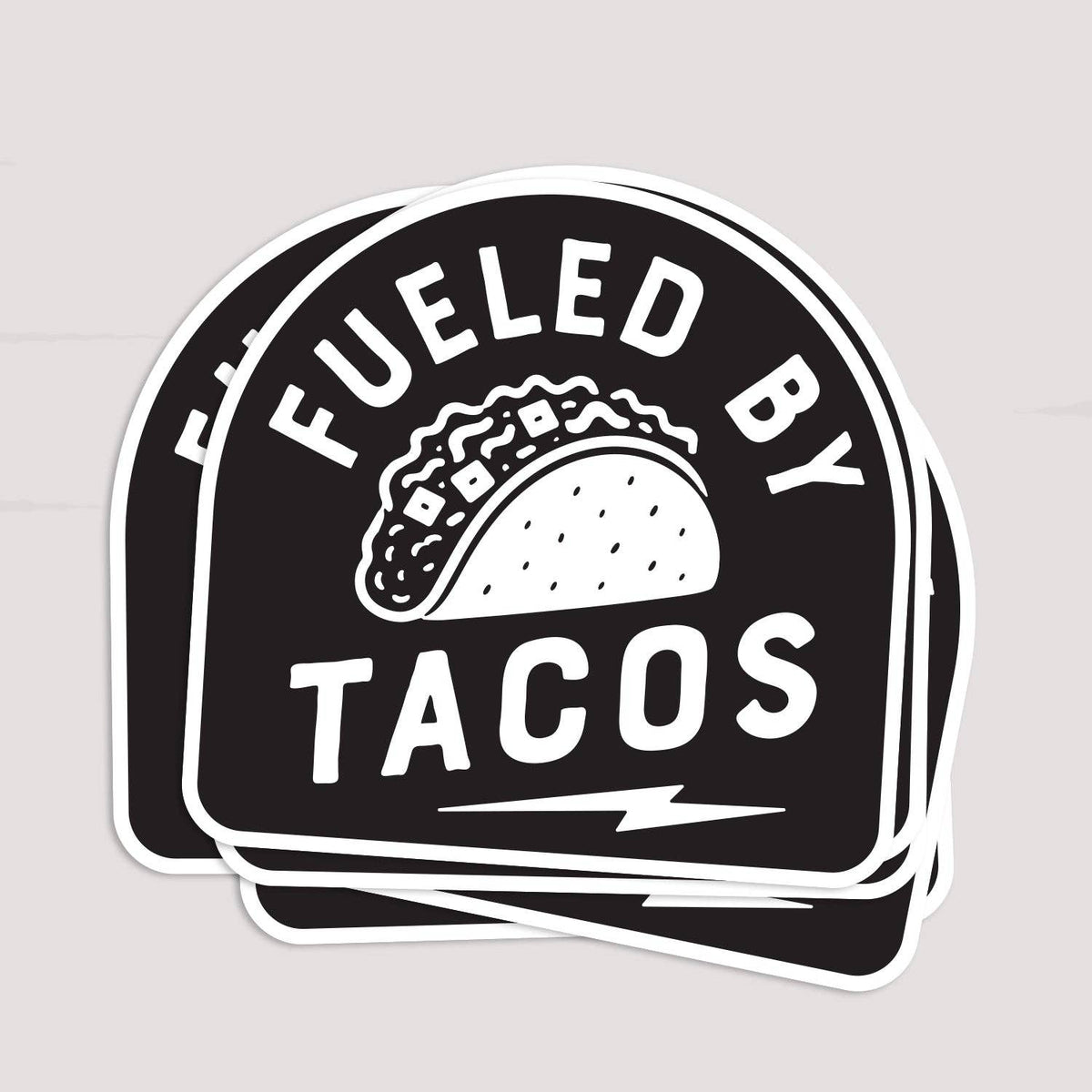 Three Fueled By Tacos stickers stacked and fanned slightly on a pale grey surface.