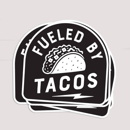 Three Fueled By Tacos stickers stacked and fanned slightly on a pale grey surface.