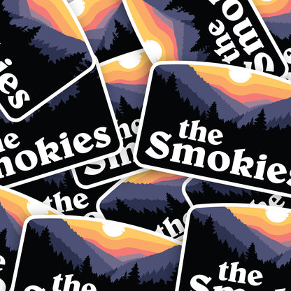 A scattered pile of The Smokies stickers overlaps edge to edge, repeating the sunset mountain design.