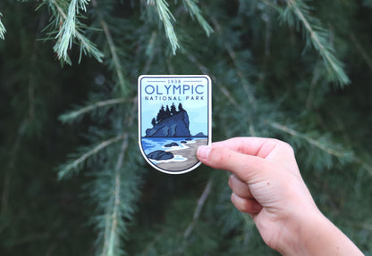 Backed further away among evergreen branches, the Olympic National Park sticker shows its 1938 arch and shoreline scene.