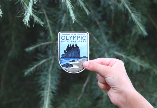 Backed further away among evergreen branches, the Olympic National Park sticker shows its 1938 arch and shoreline scene.
