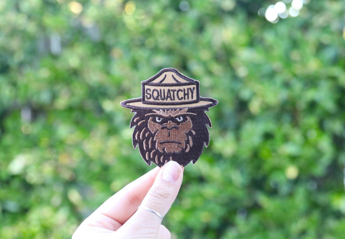 Held at arm's length in daylight, the Squatchy patch catches sun along its tan hat band.