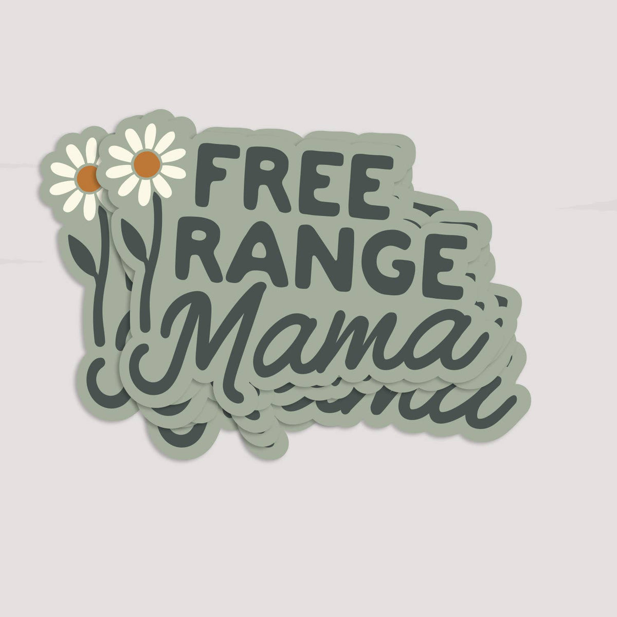 A small stack of Free Range Mama stickers fans out on a soft grey surface, daisies overlapping.