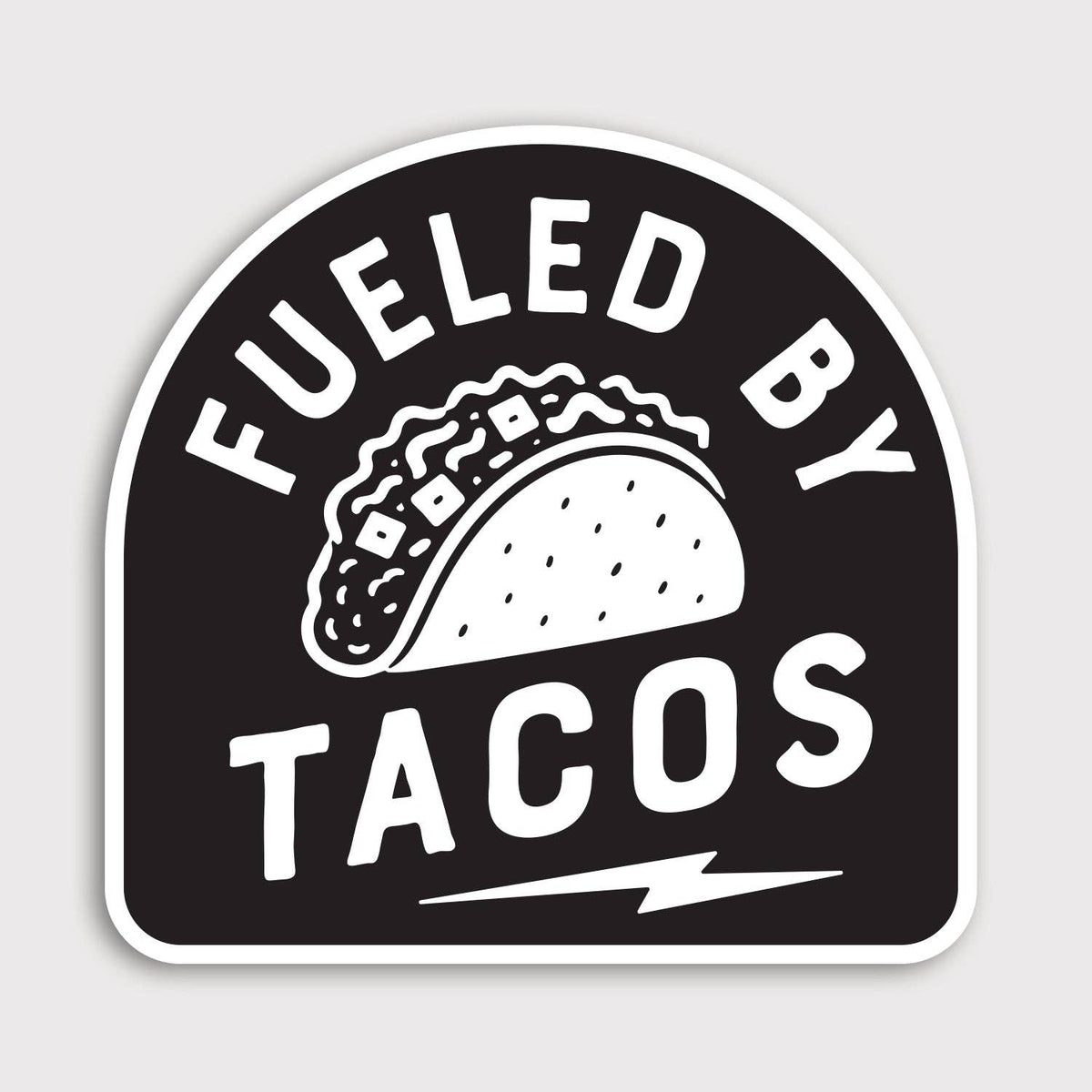 Black and white Fueled By Tacos sticker with an arched badge shape, taco drawing and lightning bolt below.