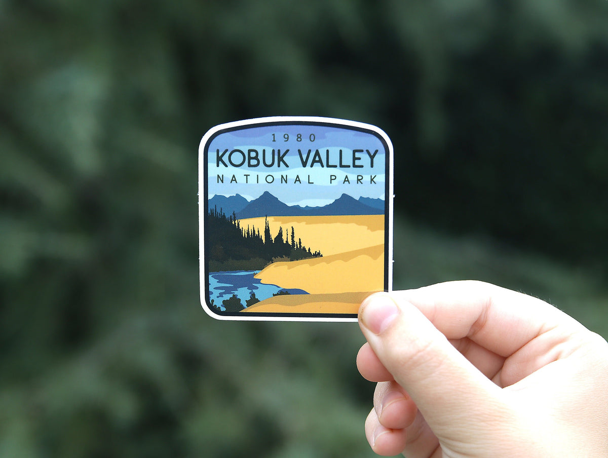 Held further back against dark green foliage, the Kobuk Valley National Park sticker shows its dunes and river.