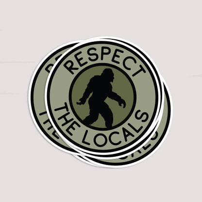 Two Bigfoot Respect The Locals stickers overlap in a stack on a soft pink surface.