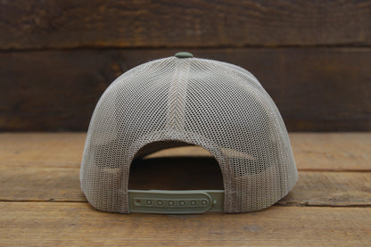 Back of an olive Yellowstone trucker hat, tan mesh and green snap strap against rough sawn wood.