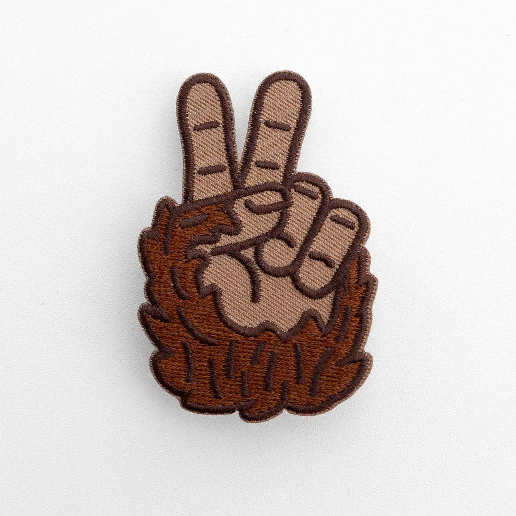 Close up on white, the Bigfoot Peace Patch shows brown stitched fur and two raised fingers.