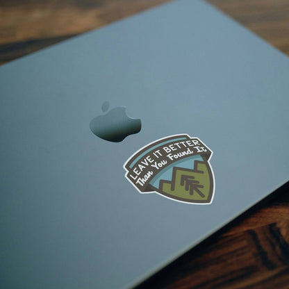 On the lid of a blue laptop, the Leave It Better Than You Found It sticker sits below the Apple logo.