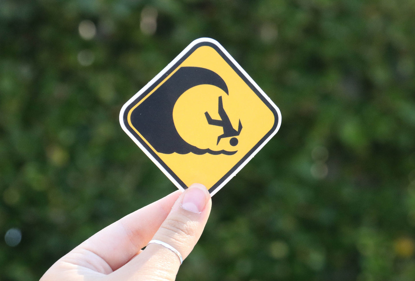 Held further back, the High Surf Warning sticker shows its full black wave and tumbling surfer in daylight.