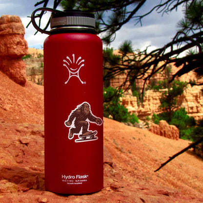 A red insulated water bottle wears the Later Skater Bigfoot sticker with red rock canyon walls behind.