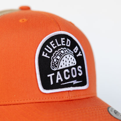 A close crop on the orange crown shows the taco patch lettering and white edge stitching of the trucker hat.