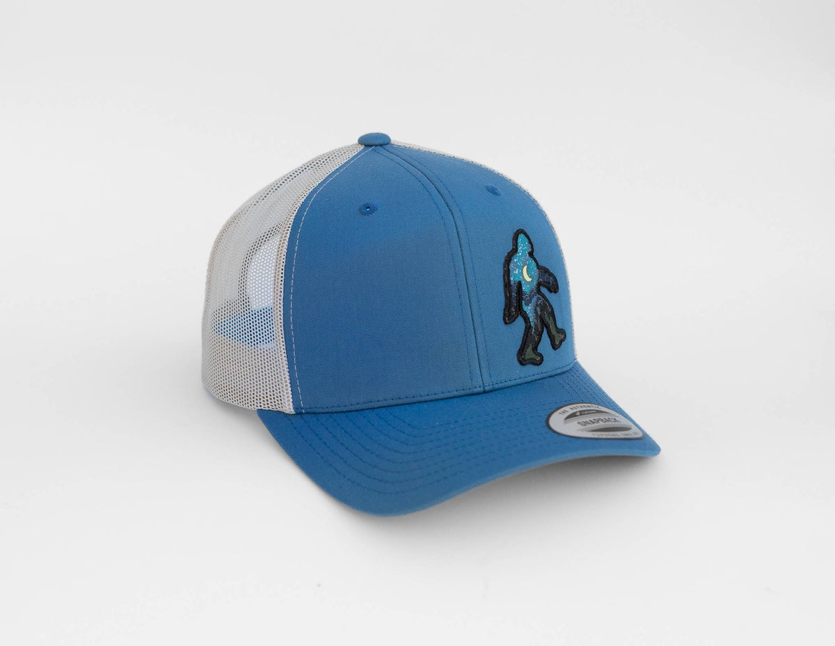 Blue and white Bigfoot Night Sky trucker hat seen from the side, patch stitched on the blue front panel.