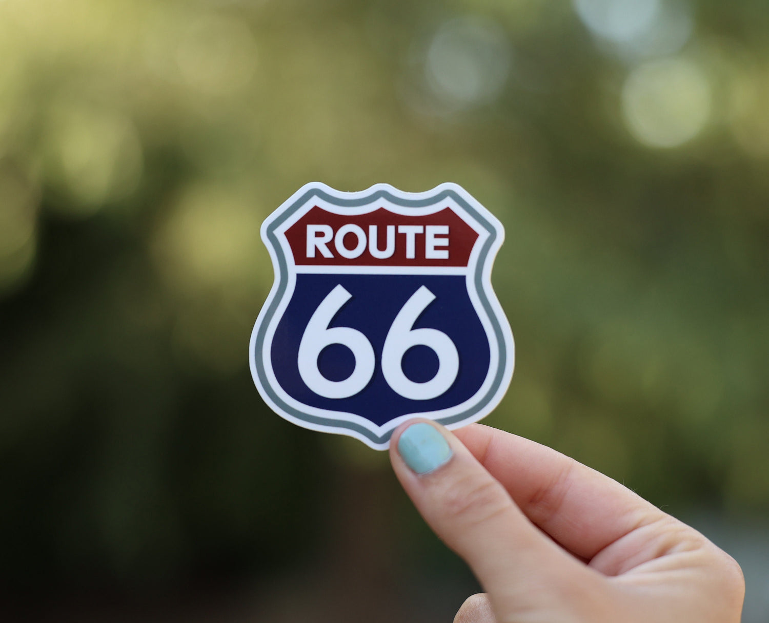 Pulled back a little, the Route 66 shield sticker sits smaller in the frame above the same fingertips.