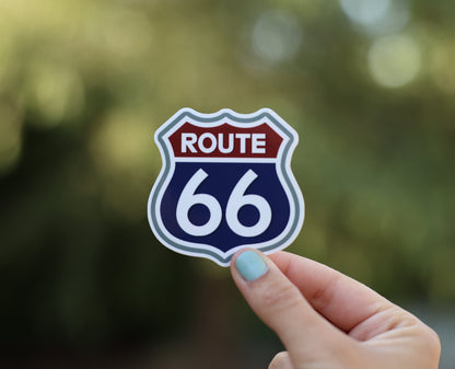 Pulled back a little, the Route 66 shield sticker sits smaller in the frame above the same fingertips.