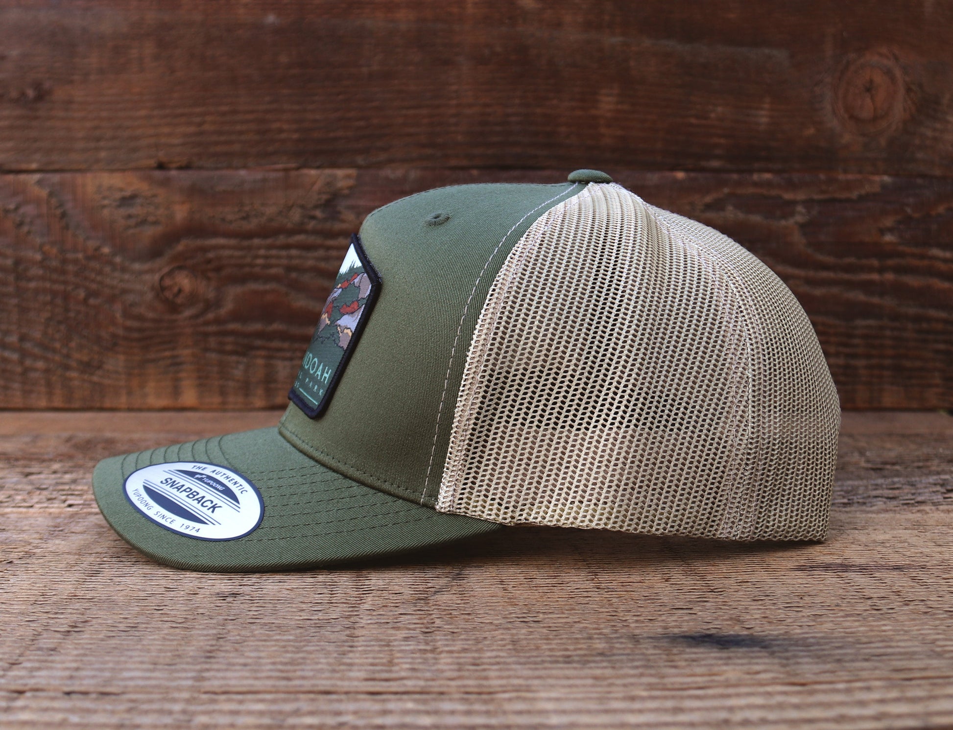 Side profile on wood boards, the Shenandoah National Park trucker hat pairs an olive crown with khaki mesh.