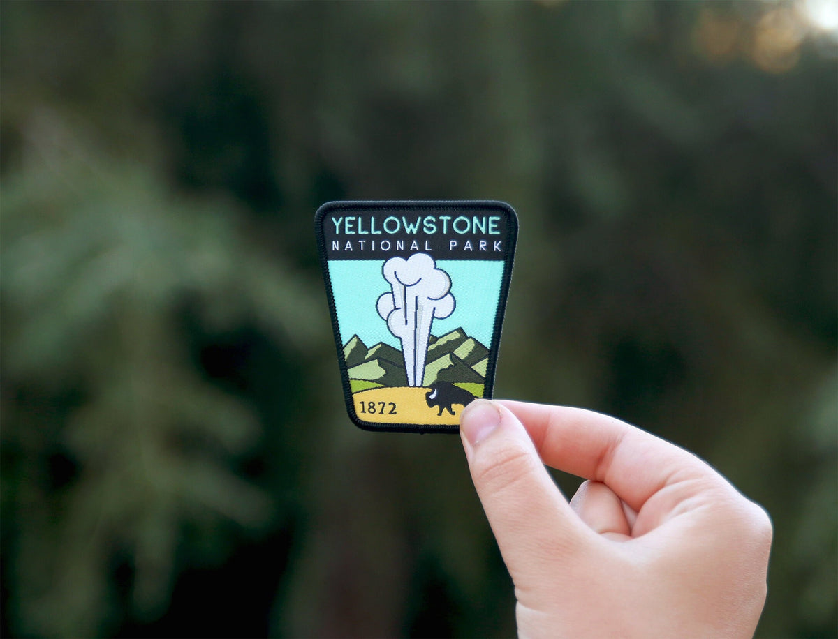 Held at arm's length against a green tree line, the Yellowstone National Park patch catches soft daylight.