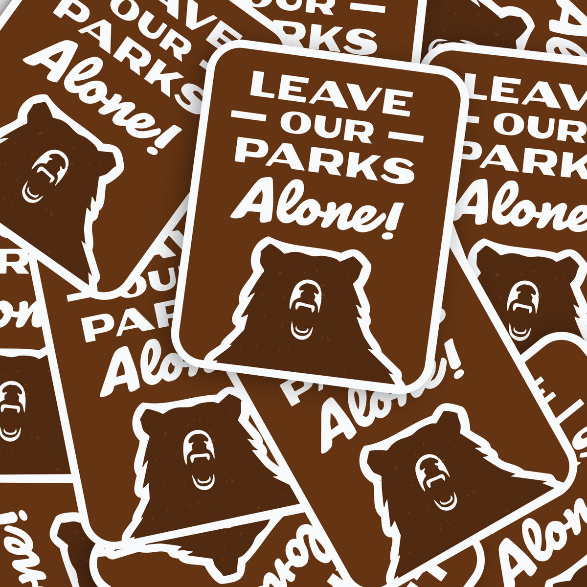 A pile of Leave Our Parks Alone stickers overlaps itself, each one printed with the same roaring bear.