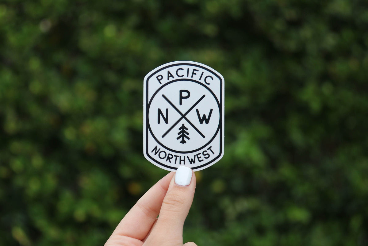 Held a little farther back against a leafy hedge, the black and white PNW Compass sticker fills the frame.