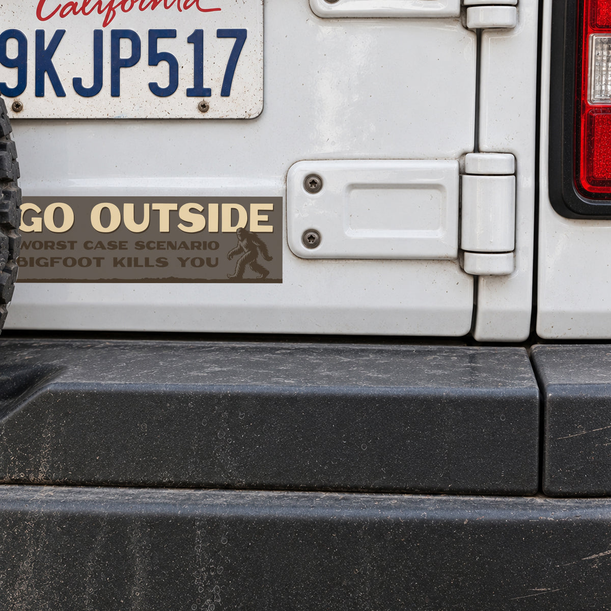 On a white Jeep's tailgate, the Go Outside Worst Case Scenario Bigfoot Kills You sticker sits near the hinge.