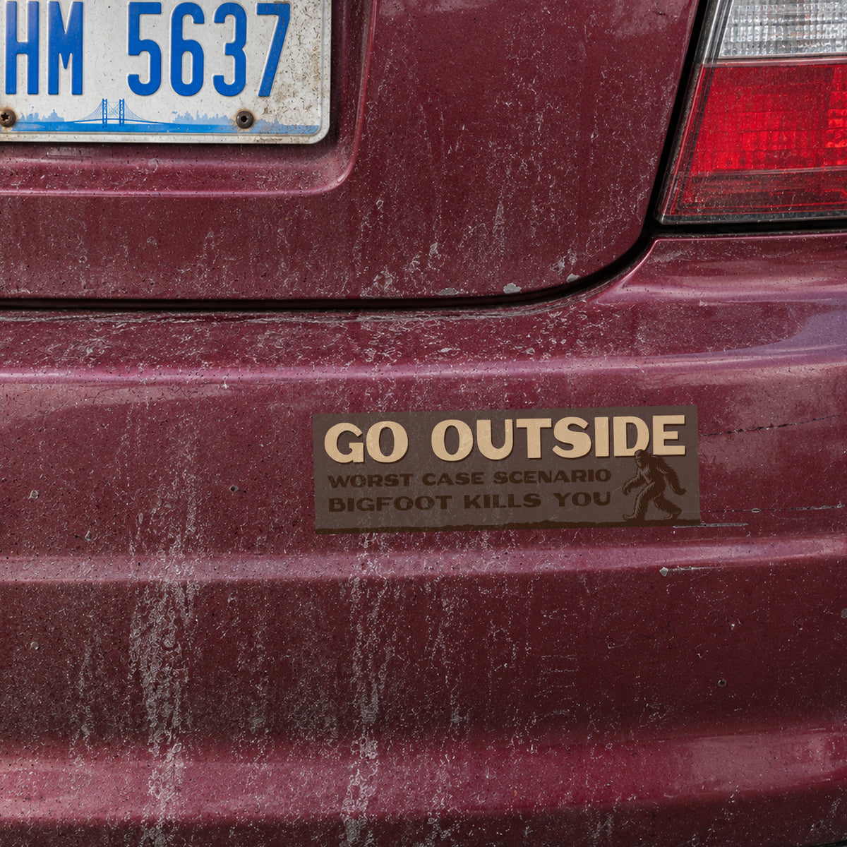 Below a rusty license plate, the Go Outside Worst Case Scenario Bigfoot Kills You sticker sits on a maroon bumper.