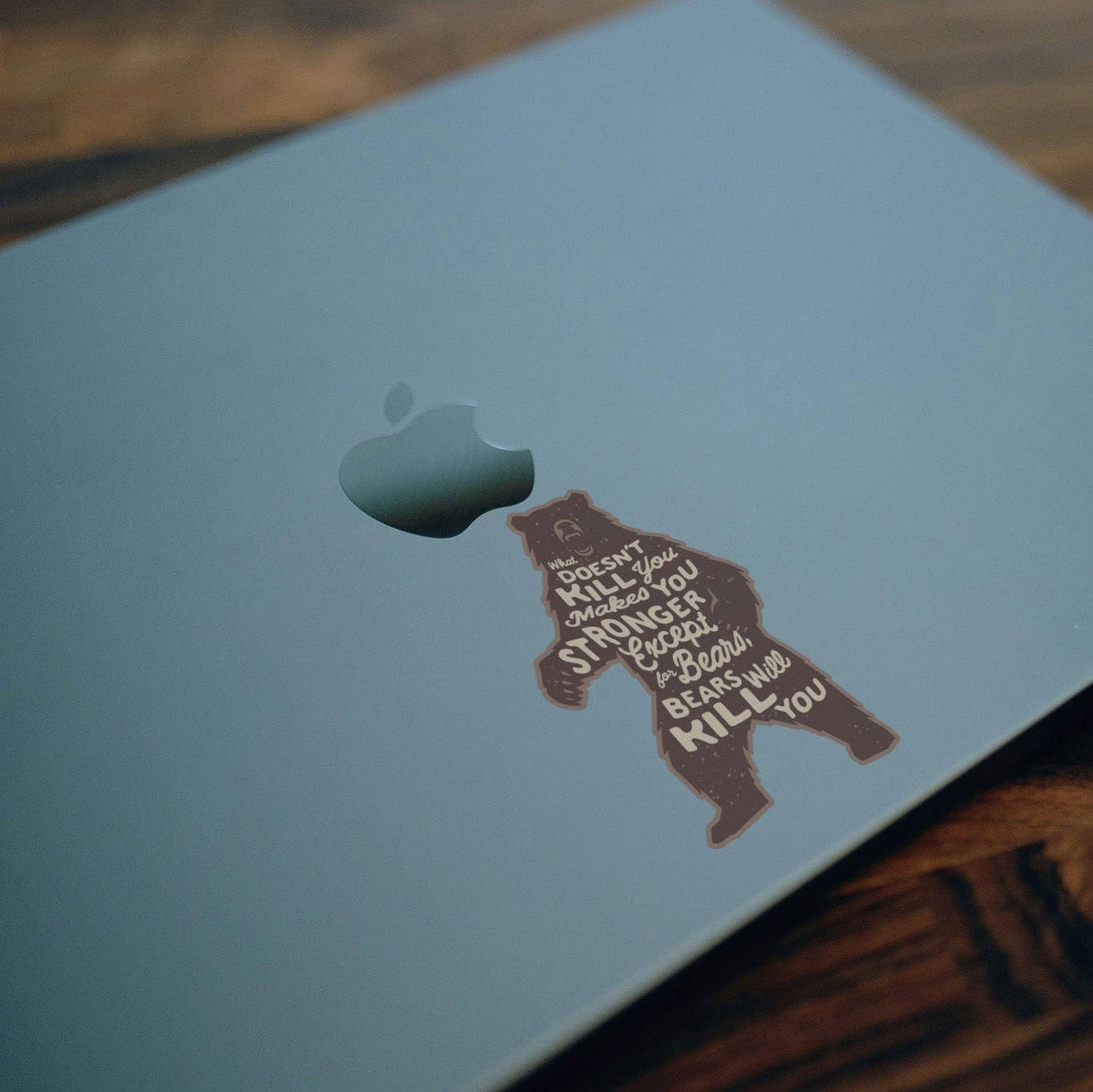 Stuck beside the logo on a pale blue laptop lid, the Bears Will Kill You sticker sits on a wood desk.