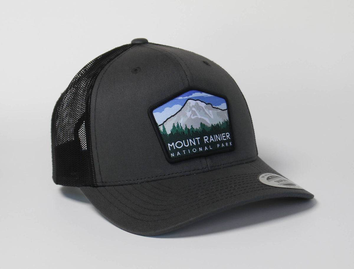 Charcoal Mount Rainier National Park trucker hat angled on white, its mountain patch stitched across the front panel.