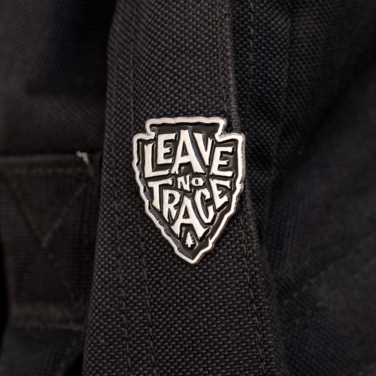 Fastened to a black canvas strap, the Leave No Trace pin stands out in silver against the dark fabric.