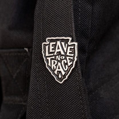Fastened to a black canvas strap, the Leave No Trace pin stands out in silver against the dark fabric.
